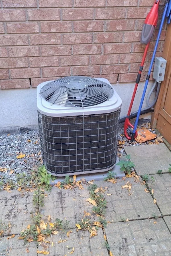 A modern, cube-shaped heat pump condenser unit sitting on a concrete slab beside the house.