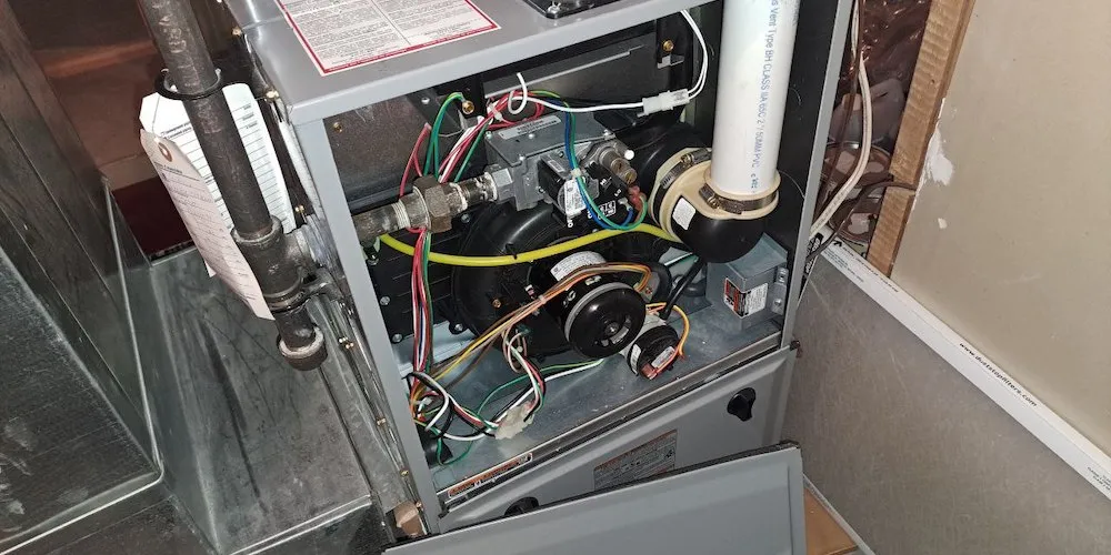 A close-up, internal view of a high-efficiency residential gas furnace with the front panel removed. It shows the inducer motor, gas valve assembly, and various electrical wiring and sensors.