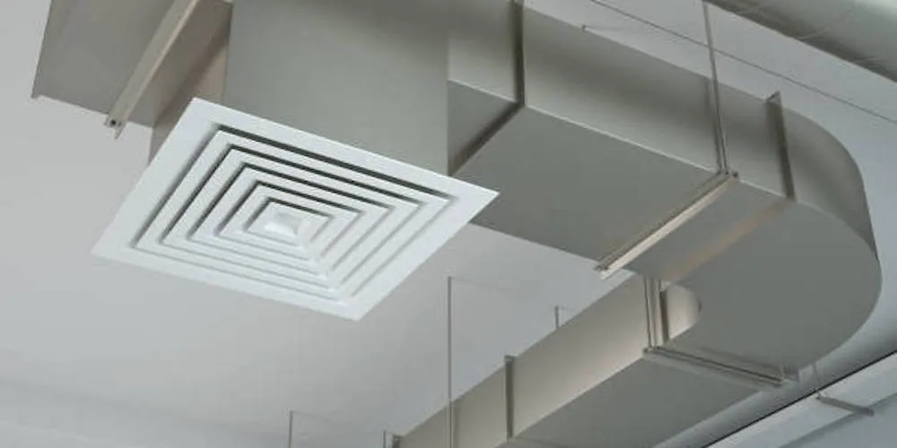 Low-angle shot of a white square ceiling diffuser connected to a rectangular galvanized steel HVAC duct with a curved 90-degree elbow.